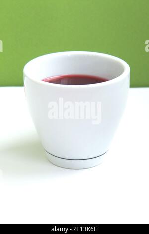 Red hibiscus tea in a white cup on green background. Side view Stock Photo