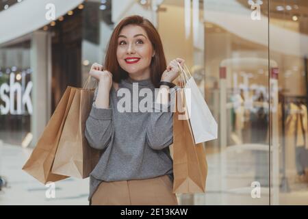 Young beautiful happy woman smiling joyfully, holding her shopping bags, enjoying sale at the mall, copy space. Excited attractive female cusotmer at Stock Photo