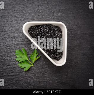 black grainy caviar of paddlefish fish in a white ceramic bowl, black background, top view Stock Photo