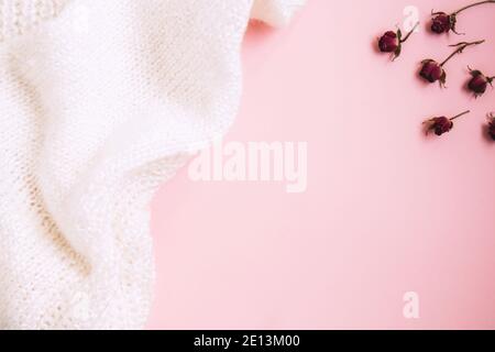 Valentine's Day background. Miniature red rose buds and white knitted fabric on pastel pink background. Valentines day concept. Flat lay with copy spa Stock Photo