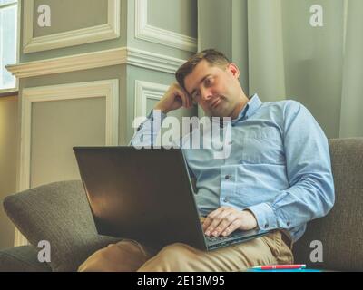 Tired sad man sitting at home on the couch with a laptop. Stock Photo