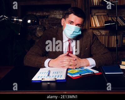 Portrait of a businessman in a medical mask sitting at the table. Stock Photo