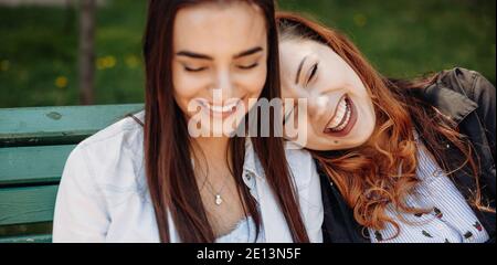 Plump red haired woman lying on her friend in the park on the bench and smile Stock Photo