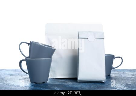 Blank coffee bags and cups on table against white background Stock Photo