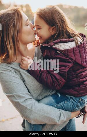 Careful mother kissing her daughter and holding her outside in a sunny day Stock Photo