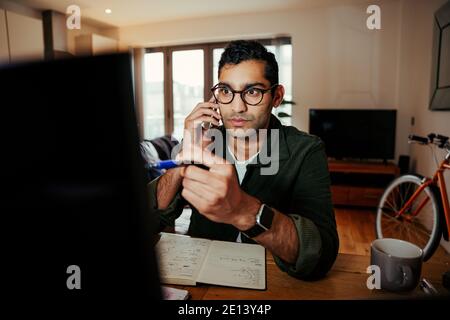 Mixed race business man pointing to laptop screen while on the telephone with client explaining business processes  Stock Photo