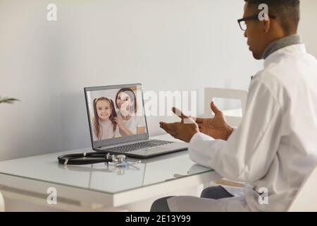 Family doctor sitting at table with laptop and talking to mother and her daughter Stock Photo