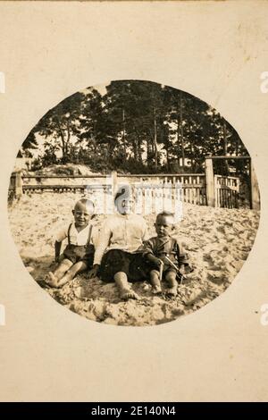 Germany - CIRCA 1920s: Group photo of tree small kids sitting on ground in garden. Vintage archive Art Deco era photography Stock Photo