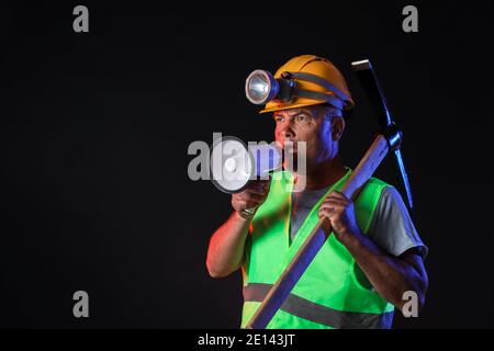 Protesting miner man with megaphone on dark background Stock Photo