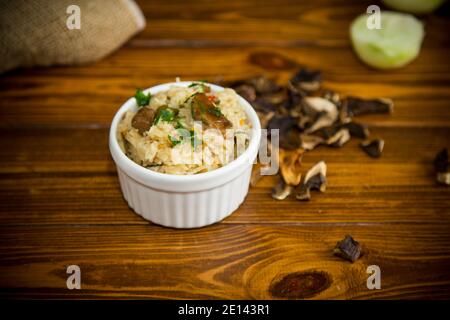 cooked rice with dried forest mushrooms, in a bowl on a wooden table Stock Photo