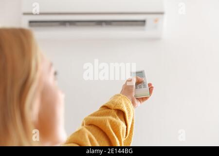 Woman setting air conditioner to heat at home. Concept of heating season Stock Photo