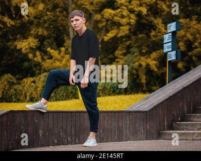 Black t-shirt template on a guy standing on a blurred background in the park, blank stylish clothes, for design presentation, print. Mockup of men's b Stock Photo