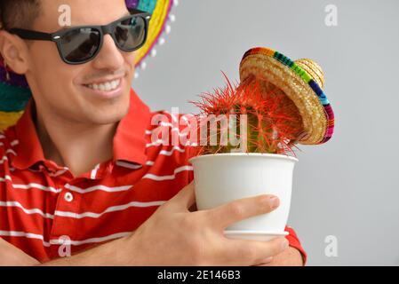 Handsome young man in sombrero hat and with cactus on grey background Stock Photo