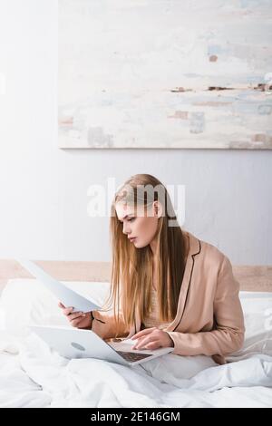 young woman in silk robe looking at document neat laptop on bed Stock Photo