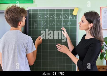 Male teenager student with teacher near school chalk board at math lesson Stock Photo