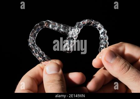 The guy holds in his hand transparent aligners plastic braces retainers for straightening teeth on a black background Stock Photo