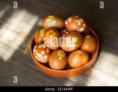 Easter eggs decorated with natural leaves and boiled in onions peels on the plate on wooden background. Easter concept. Stock Photo
