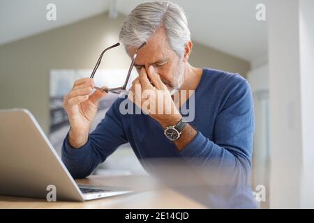 Senior man having migraine while working on laptop computer Stock Photo