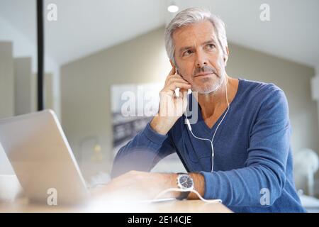 Senior man working on laptop and using earphones for virtual meeting Stock Photo