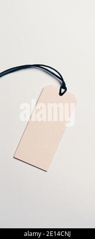 The price tag made of cardboard is empty without inscriptions on a light background. Light falls from one side, there is a shadow. Stock Photo