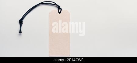The price tag made of cardboard is empty without inscriptions on a light background. Light falls from one side, there is a shadow. Stock Photo