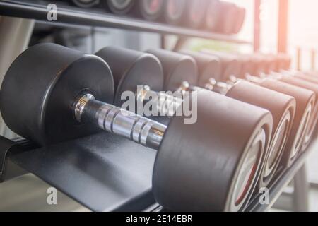 Black dumbbell set. Close up many metal dumbbells on a rack in the sports fitness center. Stock Photo