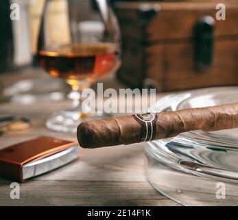 Tobacco and alcohol. Cigar and brandy on a wooden table, closeup view. Cuban quality cigar and rum, smoking and drinking luxury lifestyle Stock Photo