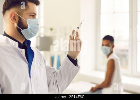 Young doctor in face mask preparing syringe before giving antiviral injection to patient Stock Photo