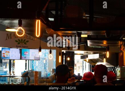 Mojo Market- Cape Town, South Africa - 16/12/2020 Artistically shaped neon light bulbs hanging over a kitchen in trendy restaurant in Mojo Market. Stock Photo