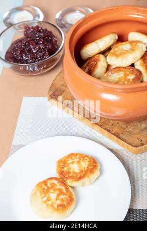 sweet cottage cheese pancakes in a plate and a clay pot, with jam on a server table Delicious cottage cheese dessert. High quality photo Stock Photo