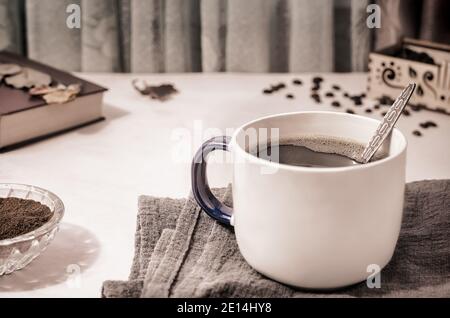 On the table on a napkin is a Cup of black coffee, next to coffee beans, ground coffee. Front view, close-up. Stock Photo