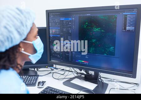 Researcher looks at results from microscope on PC monitor while searching for Covid-19 vaccine Stock Photo