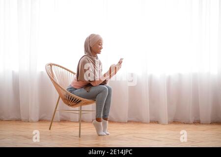 Millennial black lady in hijab using cellphone at home, working or studying remotely, free space Stock Photo