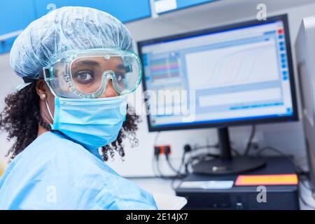 African woman as researcher in the laboratory at the computer analyzing data after experiment on Covid-19 vaccine research Stock Photo