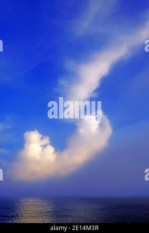 Diagonal cloud seascape against blue sky with light reflecting on the sea Stock Photo