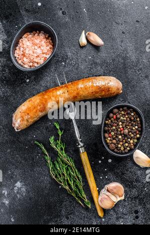 Sausage barbecue fried with spices and herbs on a meat fork. Top view. Black background Stock Photo
