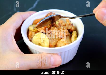 Hand Scooping Banana Walnut Bread Pudding in a Ceramic Bowl on Black Table Stock Photo