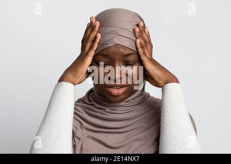Upset Black Islamic Lady In Hijab Having Strong Headache, Touching Temples Stock Photo