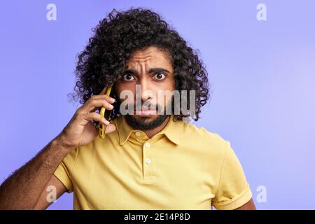 male is upset for mistake, man having talk on phone with partner, in shock, isolated purple background Stock Photo