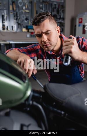 mechanic using flashlight and screwdriver during diagnostics of motorbike Stock Photo