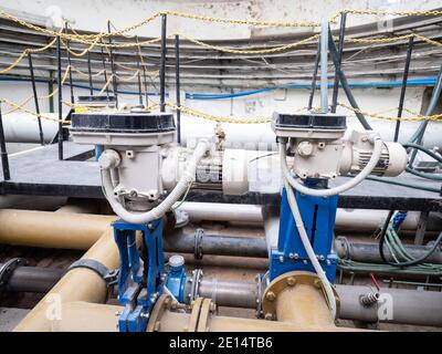 Two knife gate valves on yellow sludge pipeline. System controlled remotely  by servo drive engine. Underground shaft. Stock Photo