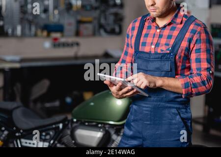 cropped view of technician in overalls using digital tablet in workshop Stock Photo