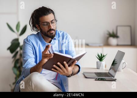 Young Arab Freelancer Guy Checking Working Schedule In Notepad At Home Stock Photo