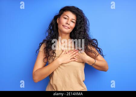 woman holding hands on chest, expressing gratitude, you are welcome gesture. isolated blue background Stock Photo