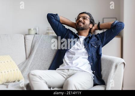 Relaxed smiling arab guy leaning back on couch, relaxing at home Stock Photo