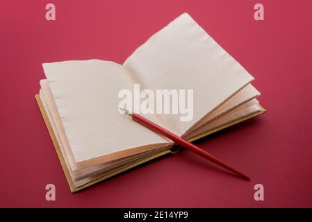 Vintage red pen with gold nib on open antique leather hardcover notebook  on cardinal red color background Stock Photo