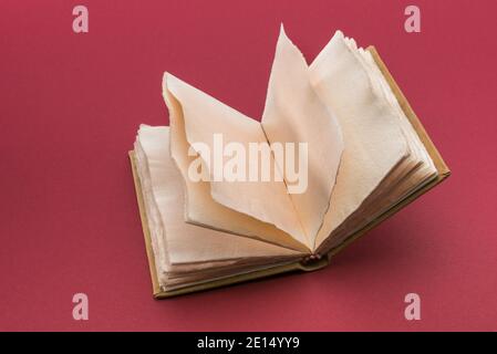 Open antique style book with pages of rough paper with jagged edges, antique leather hardcover notebook  on cardinal red background Stock Photo