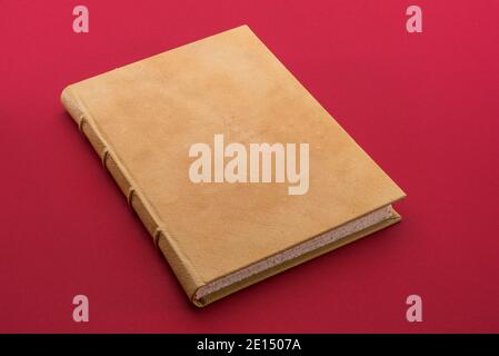 Antique book with light brown leather hardcover on cardinal red background Stock Photo