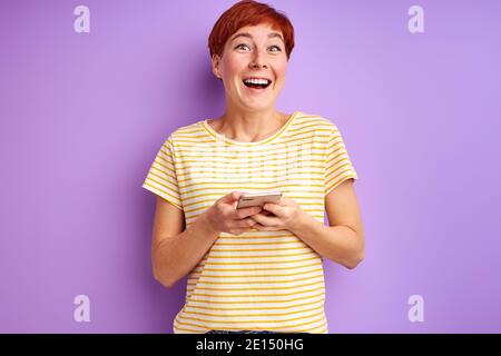 short haired female enjoy chatting with friend, she uses smartphone isolated over purple background Stock Photo