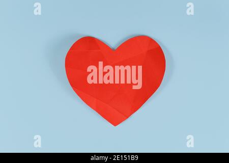 Broken red paper heart with folding lines on blue background. Concept for broken or sick heart Stock Photo